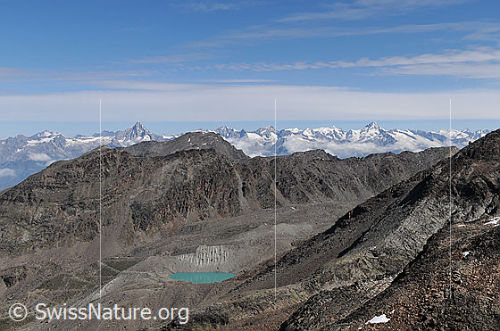 Foto: Blick vom Jegihorn zu den Berner Alpen. Über der Bergkette liegen Wolkenfelder. In der Moränenlandschaft im Vordergrund ist ein türkisfarbener Bergsee zu sehen.