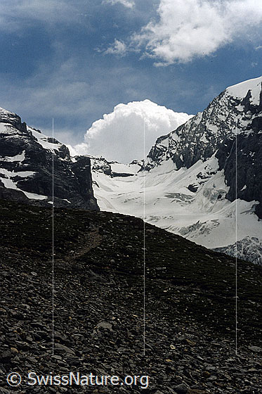 Foto: Gamchilücke und Gamchigletscher mit Geröllhalde im Vordergrund. Am Himmel sind Kumuluswolken zu sehen. Aufnahme ab Dia.