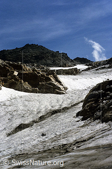 Foto: Helsenhorn und Helsengletscher mit Felsen, welche aus dem Eis ragen. Am Himmel sind Schleierwolken zu sehen. Aufnahme ab Dia.