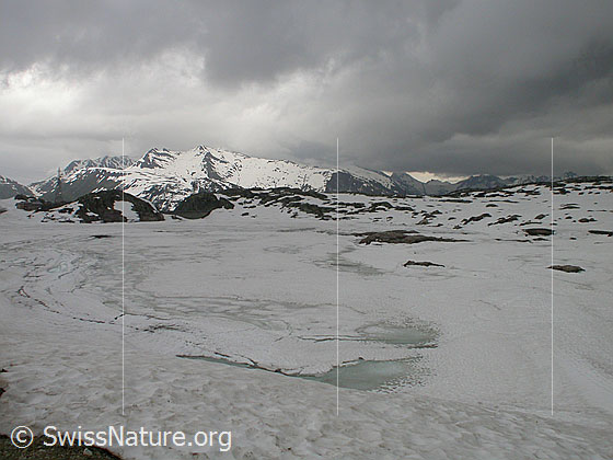 Foto: Grimselpass: Blick über den mit Eis bedeckten Totesee Richtung S. Am Himmel dunkle Wolken.