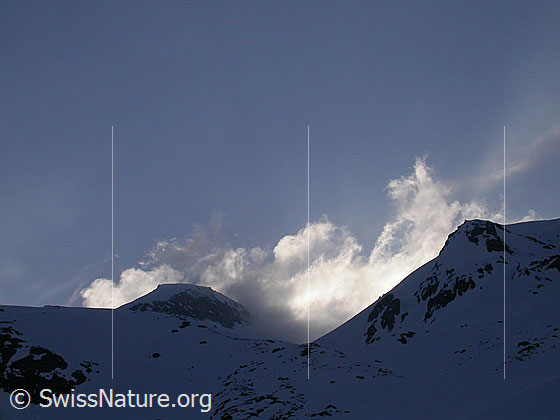 Foto: Blick vom Mässersee Richtung Hotäl.  Wolkenfetzen und Schneefahnen über dem oberen Teil des Hotäl im Gegenlicht. Die Aufnahme entstand am frühen Morgen.