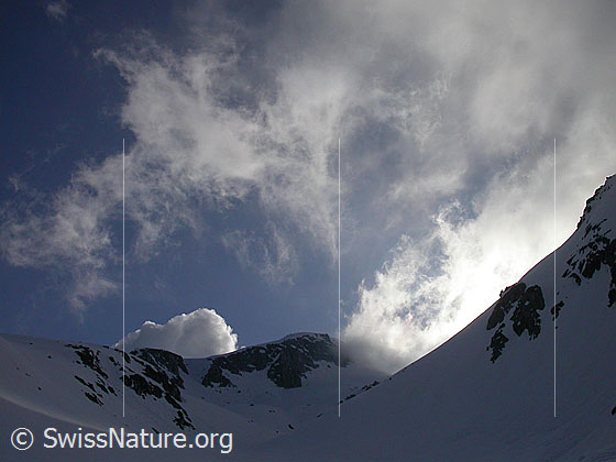 Foto: Wolkenfetzen und Schneefahnen über dem oberen Teil des Hotäl im Gegenlicht. Die Aufnahme entstand am frühen Morgen.
