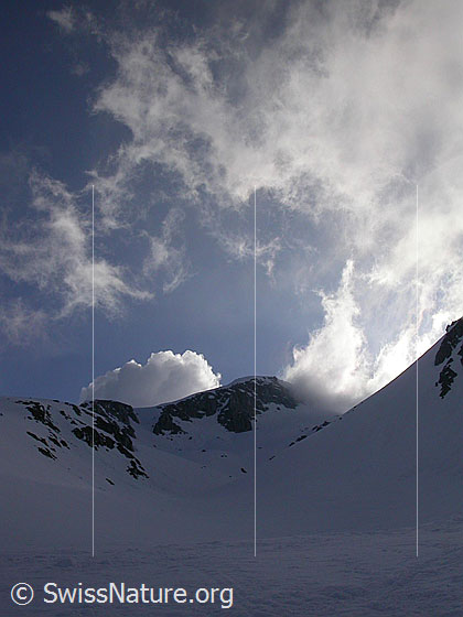 Foto: Wolkenfetzen und Schneefahnen über dem oberen Teil des Hotäl im Gegenlicht. Die Aufnahme entstand am frühen Morgen.