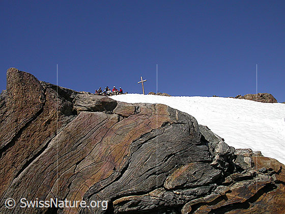 Foto: Gipfel des Ofenhorn. Auf dem Gipfel sitzt eine Gruppe Alpinisten. Im Vordergrund: Fels mit interessanter Schichtung.