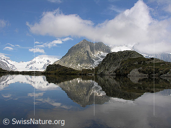 Foto: Blick über einen kleiner Bergsee am Eggishorn Richtung Jungfraujoch mit Spiegelung und Wolken.