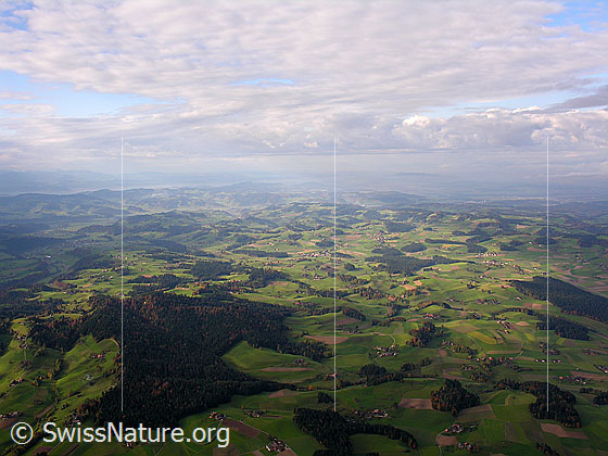 Foto: Luftaufnahme Emmental. Tiefblick auf die Hügellandschaft mit Wäldern und Streusiedlung. Darüber sind Wolkenfelder zu sehen.