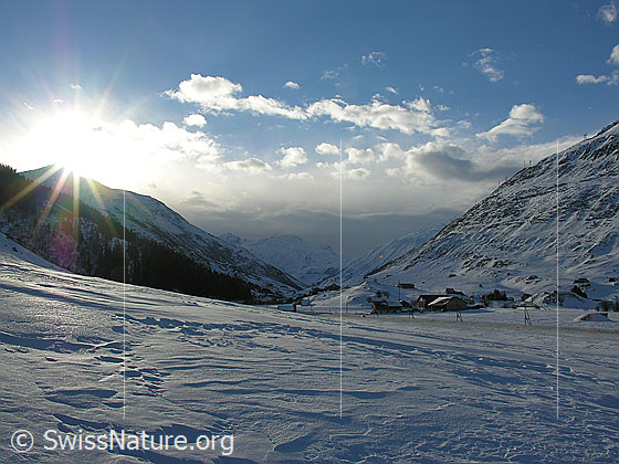 Foto: Blick von Andermatt Richtung Hospental mit Sonne über dem Winterhorn, aufziehende Wetterfront Wolken und Struktur im Schnee.