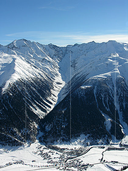 Foto: Tiefblick vom Bächigalen auf das Dorf Reckingen und ins Blinnental mit Licht und Schatten im Taleinschnitt. Im Hintergrund sind Blinnenhorn, Turbhorn und Rappehorn zu sehen. Die Schutzwälder an den Bergflanken sind in der schneebedeckten Landschaft gut erkennbar.