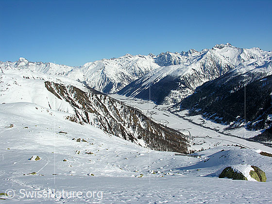 Foto: Tiefblick vom Bächigalen auf die Dörfer Obergesteln, Ulrichen und Geschinen im schneebedeckten Talgrund des Obergoms. Im Hintergrund sind Galenstock, Tällistock, Muttenhörner, Saashörner, Pizzo Rotondo, Blashorn, Galmihorn, Mittaghorn und Pizzo Gallina zu sehen.