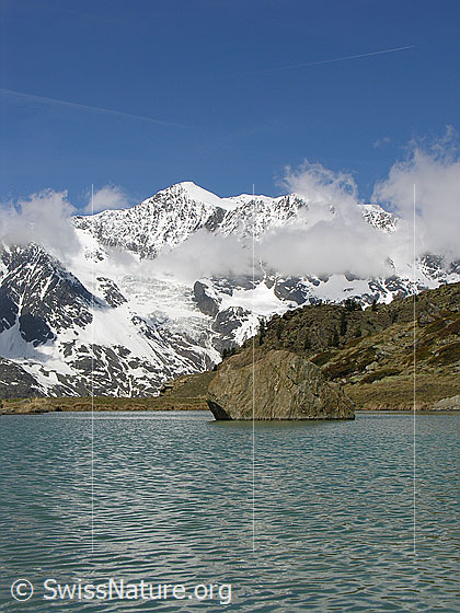 Foto: Balfrin mit Wolken. Davor ein Bergsee (Farbe: türkis). Im Bergsee ein Felsblock.