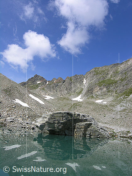 Foto: Mättitalsee mit Spiegelung eines Felsblocks, des Rothorns und der steinigen Umgebung des Mättitals.