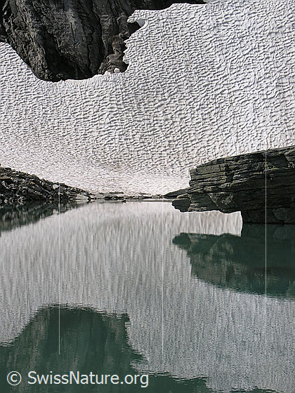 Foto: Ein Schneefeld und ein Felsblock spiegeln sich im Mättitalsee.