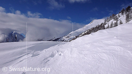 Foto: Schneeverwehung in Winterlandschaft und Wolkenstimmung über den Bergen.