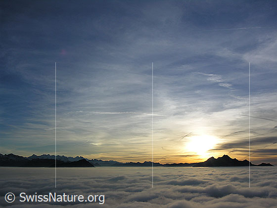 Foto: Abendstimmung mit Silhouette des Pilatus und kompaktem Nebelmeer. Im Horizont ist die Bergkette der Berner Alpen und davor das Stanserhorn erkennbar.
