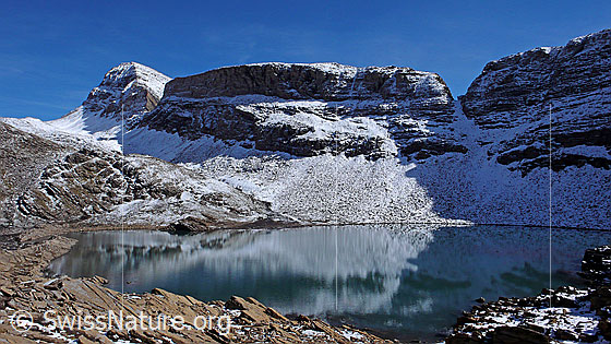 Foto: Häxeseeli, Berner Oberland, mit Spiegelung und bräunlichen Felsplatten am Ufer. Wart, Hinterbirg, Schwarzhorn, Grosse Chrinne und Kleine Chrinne sind mit erstem Schnee überzuckert.