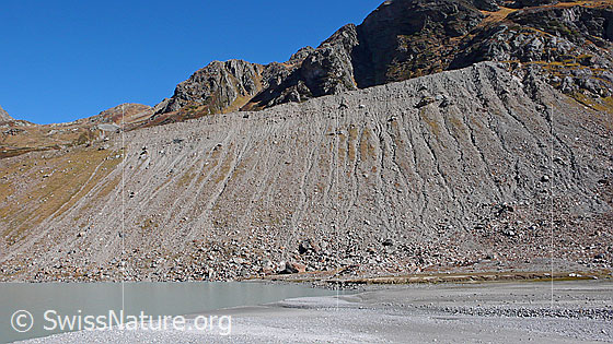 Foto: Die von Erosion gezeichnete Seitenmoräne des Steingletschers bildet das Ufer des Steinsees. Im Vordergrund sind Sand- und Kiesablagerungen des Gletschervorfeldes zu sehen.