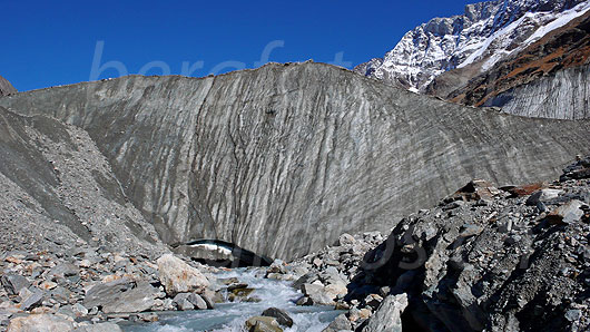 Foto: Gletschertor des Langgletschers mit mächtiger Eiswand und Gletscherbach Lonza. Darüber Herbstfarben und leicht verschneites Schinhorn.