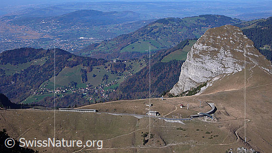 Foto: Blick vom Rochers de Naye zum Dent de Jaman und auf die Hügellandschaft mit Les Pléiades. Im Vordergrund ist ein Teil der Bahnstrecke Montreux - Rochers de Naye mit Galerien und der Bahnstation Jaman zu sehen.
