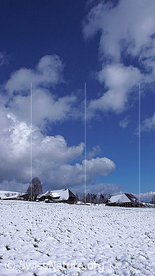 Foto: Bauernhäuser in schneebedeckter Landschaft und Wolkenstimmung.