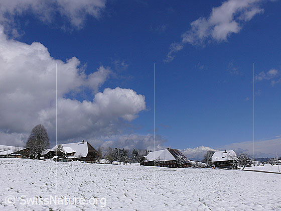 Foto: Bauernhäuser in Winterlandschaft und Wolkenstimmung.