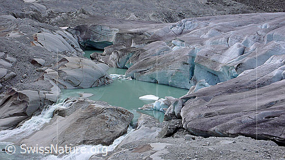 Foto: Gletschersee an Rhonequelle. Gletscherzunge und Gletschertor des Rhonegletschers münden in einen neu entstandenen Gletschersee. Der Gletscher hat auf seinem Rückzug einen Felsriegel freigelegt, an welchem sich das Wasser nun staut. Durch weiteres Abschmelzen des Gletschers wird sich der See vergrössern und könnte im Laufe der Zeit eine Naturgefahr darstellen.