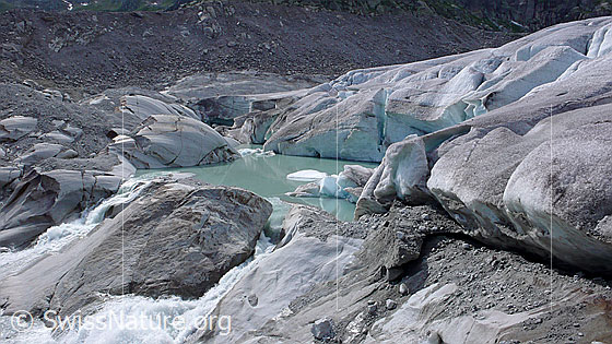 Foto: Gletschersee an der Queller der Rhone. Gletscherzunge und Gletschertor des Rhonegletschers münden in einen neu entstandenen Gletschersee. Der Gletscher hat auf seinem Rückzug einen Felsriegel freigelegt, an welchem sich das Wasser nun staut. Durch weiteres Abschmelzen des Gletschers wird sich der See vergrössern und könnte im Laufe der Zeit eine Naturgefahr darstellen.