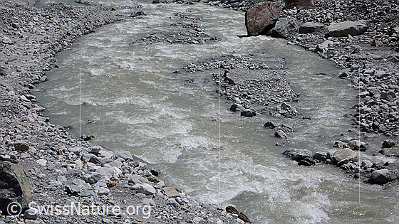 Foto: Gletscherwasser. Gletscherbach mit kleinen Inseln und Ufer aus Sand, Geröll, und Steinen.