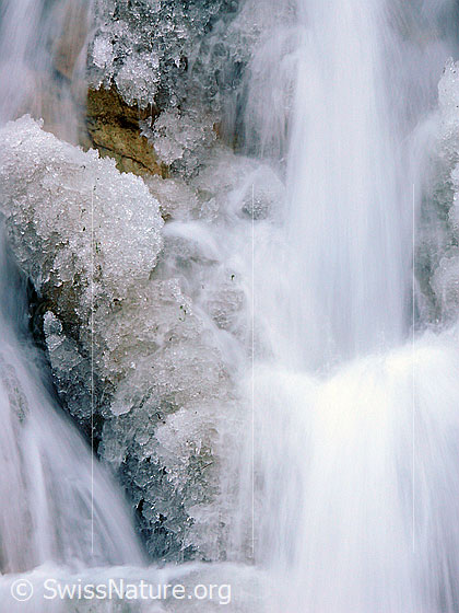 Foto: Langzeitbelichtung Wasser und Eis. Als kleiner Wasserfall fliesst das Wasser eines Bergbachs in feinen Strahlen über die mit Eisgebilden überzogenen Stufen.
