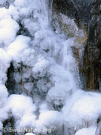 Foto: Stufe in Bergbach mit Eisgebilden und fliessendem Wasser (Langzeitbelichtung).