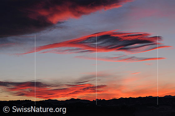 Foto: Wolkenfelder in kräftigem Morgenrot und Silhouette einer Bergkette. Die Wetterlage (Föhn) hat zur Entstehung der interessanten Wolkenformen beigesteuert.
