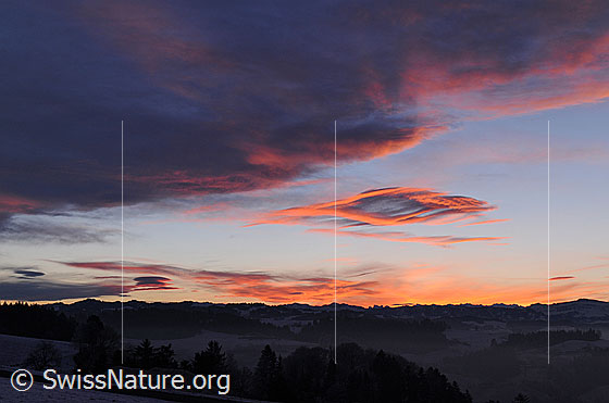Foto: Wolkenfelder in kräftigem Morgenrot und Silhouette einer Bergkette. Die Wetterlage (Föhn) hat zur Entstehung der interessanten Wolkenformen beigesteuert.