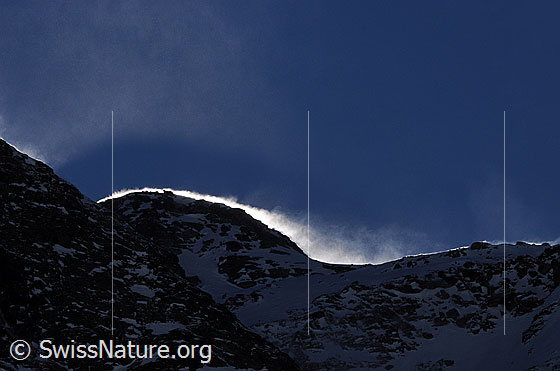 Foto: Schneeverfrachtung an Felsgrat. Im Gegenlicht ist der aufwirbelnde Schnee gut zu sehen.