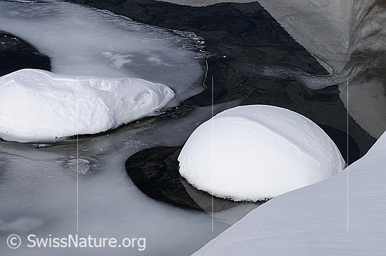 Foto: Wassereis und Schnee in einem Wasserlauf. Auf der Oberfläche des teilweise gefrorenen Gewässers befindet sich eine rund geformte Schneehaube.