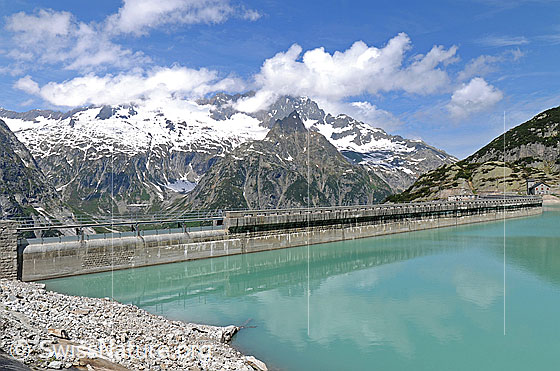 Foto: Staumauer Gelmersee mit schwacher Spiegelung und Quellwolken über dem Ritzlihorn.