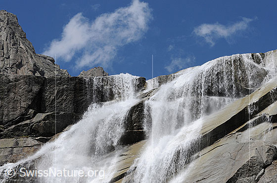 Foto: Felskante mit breitem, stiebendem Wasserfall über Stufen und Platten.