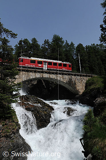 Foto: Berninabahn auf Brücke über kleine Schlucht mit tosendem Wasserfall.