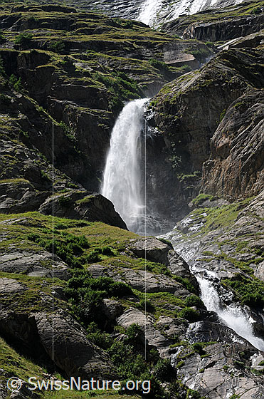 Foto: Wasserfall in urtümlicher Landschaft mit gestuften Felsen und kleiner Schlucht.