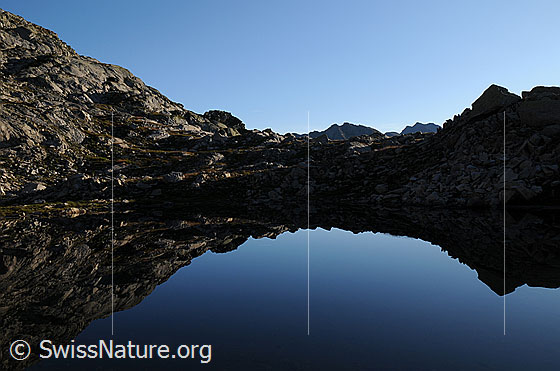 Foto: Morgenstimmung mit spiegelglattem Bergsee und Spiegelung der Felslandschaft.