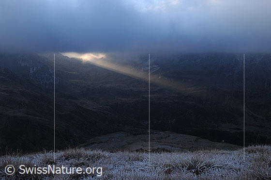 Foto: Ein Sonnenstrahl bricht durch die Wolkendecke über dem Albrunpass und verleiht der kalten Raureiflandschaft eine dramatische Stimmung.