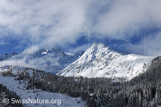 Foto: Nebelauflösung in verschneiter Berglandschaft mit Neuschnee in den Bergflanken und Wäldern.