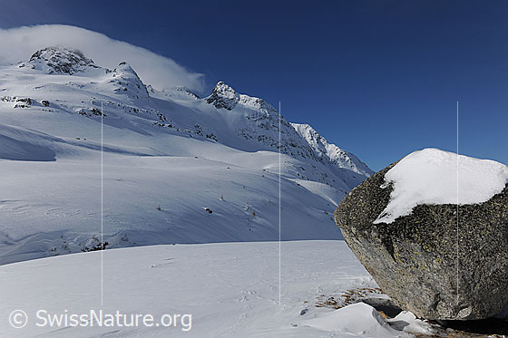 Foto: Kultstein mit Schnee. Kultstein in schneebedeckter Berglandschaft mit Bochtehorn und Seewischhorn. Über den Berggipfeln liegt eine Wolke.