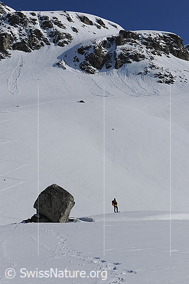 Foto: Felsblock und Mensch. Schneeschuhläuferin neben Kultstein mit Mittlenbärg im Hintergrund.