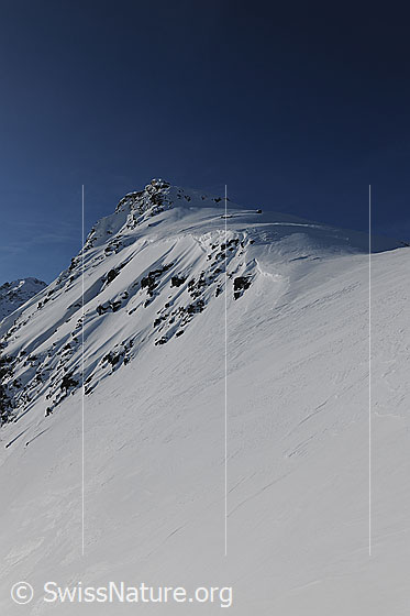 Foto: Schneebedeckter Grat am Stockhorn. Schneeverwehungen ziehen sich die Bergflanke hinunter und haben Strukturen zwischen den Felsen hinterlassen.