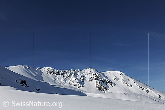 Foto: Blauer Himmel über weisser Berglandschaft. Die Schneeoberfläche im Vordergrund ist unberührt. Gipfel rechts im Bild: Hirli.