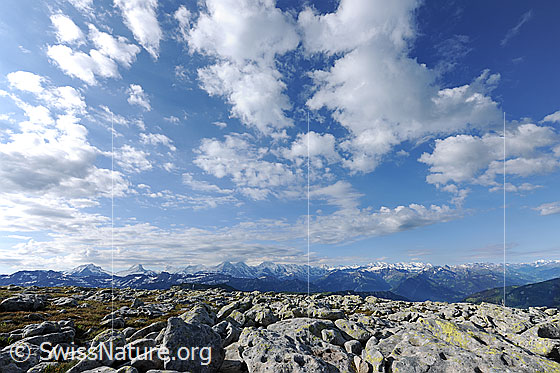 Foto: Wolkenhimmel über Hochebene mit Felsblöcken und Aussicht auf Berner Alpen.