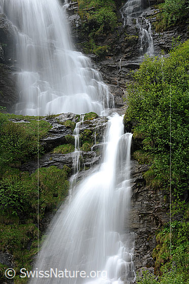 Foto: Wasserfälle in gestuftem Fels und grüner Umgebung als Langzeitaufnahme.