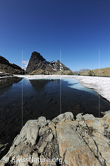 Foto: Bergsee mit Eis und Schneeresten. Im bereits offenen Wasser spiegelt sich das Rothorn.