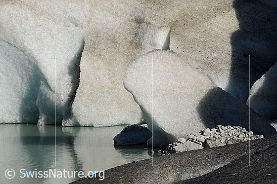 Foto: Gletscherrand und Eisklotz im Gletschersee. Im Wasser ist eine schwache Spiegelung zu sehen.