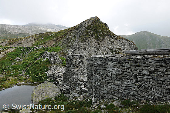 Foto: Aquädukt. Berglandschaft mit Ruine einer Wasserleitung. Teile der Pfeiler und der Steinmauer sind bereits zerfallen.