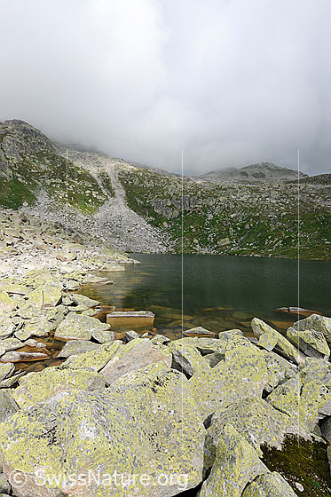 Foto: Stimmung am Lengsee mit Wolken über der Berglandschaft. Am Ufer des Bergsees ist ein Geröllkegel zu sehen.